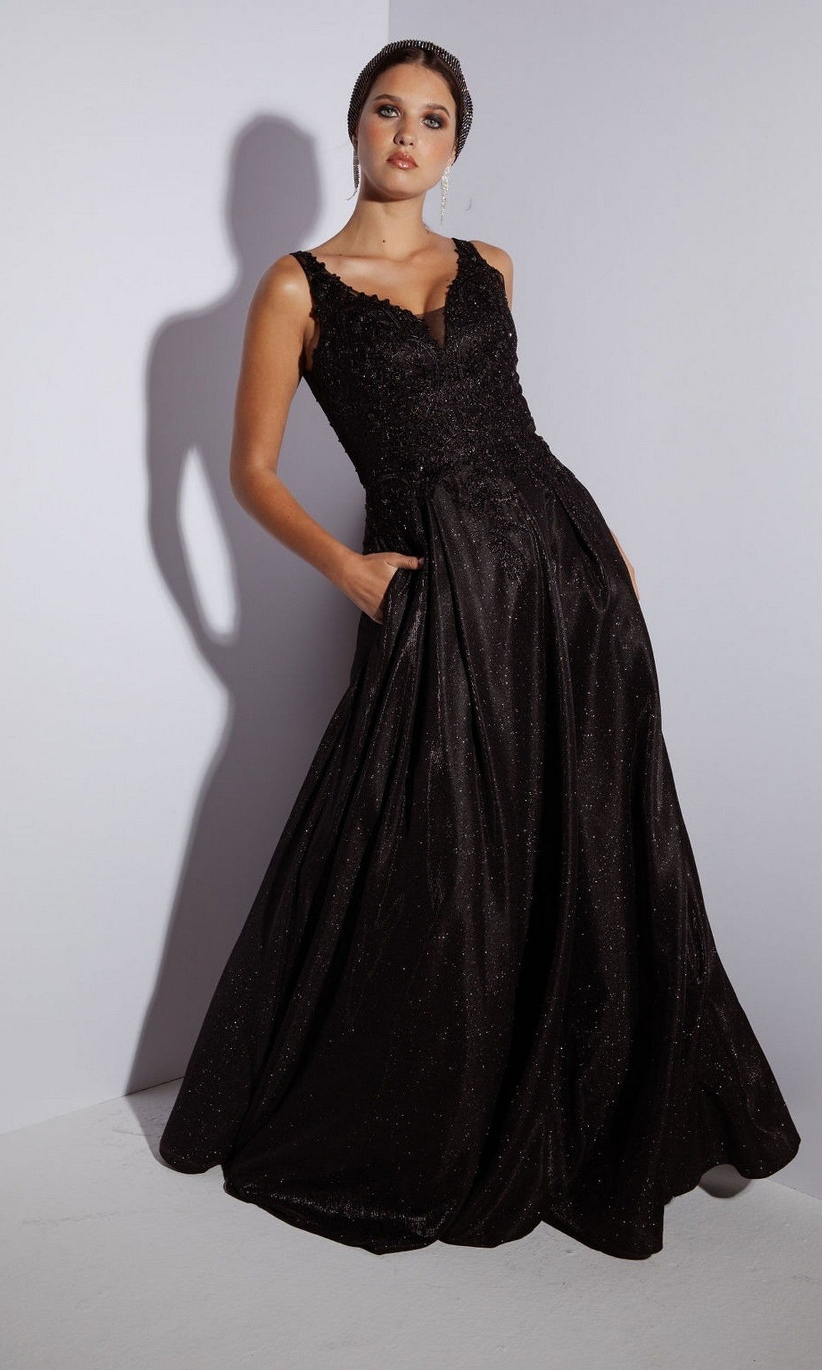 A woman in the black Eureka 9606 long prom dress, featuring a sleeveless embroidered bodice, lace details, and pockets, stands against a plain light background.